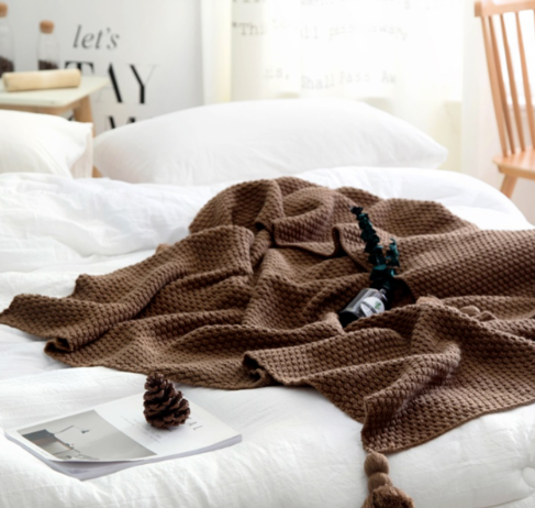 Strikket plaid med pomponer på sofa