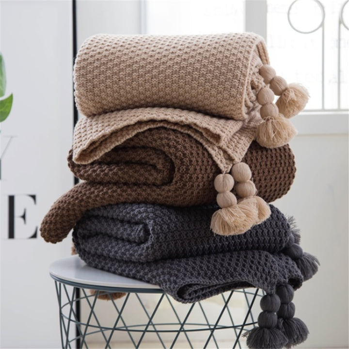 Strikket plaid med pomponer på sofa